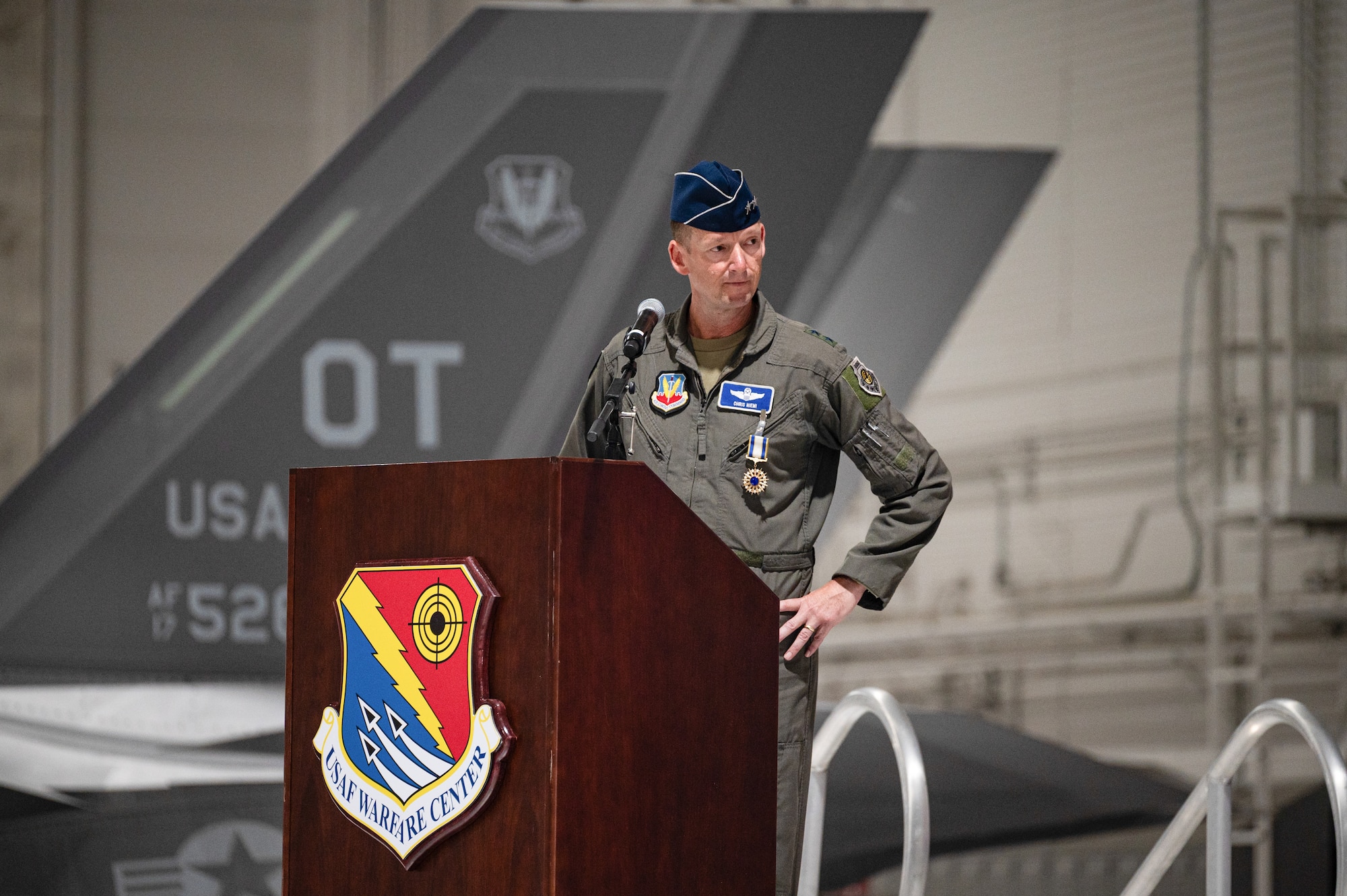 An Airman speaks at a podium. There is an F-35 in the background.