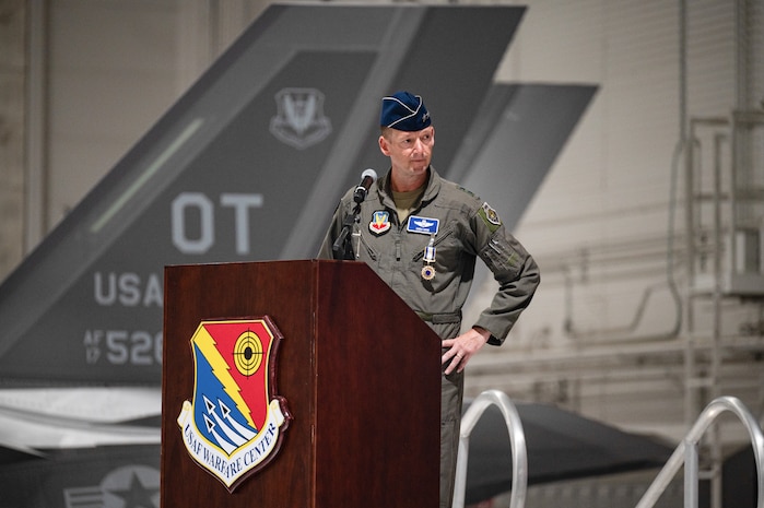 An Airman speaks at a podium. There is an F-35 in the background.