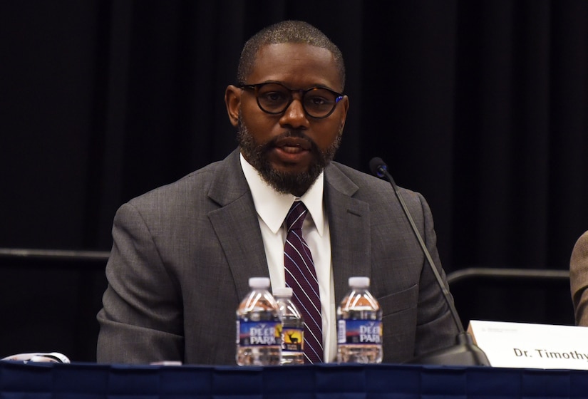 A person seated in a suit speaks to an audience.