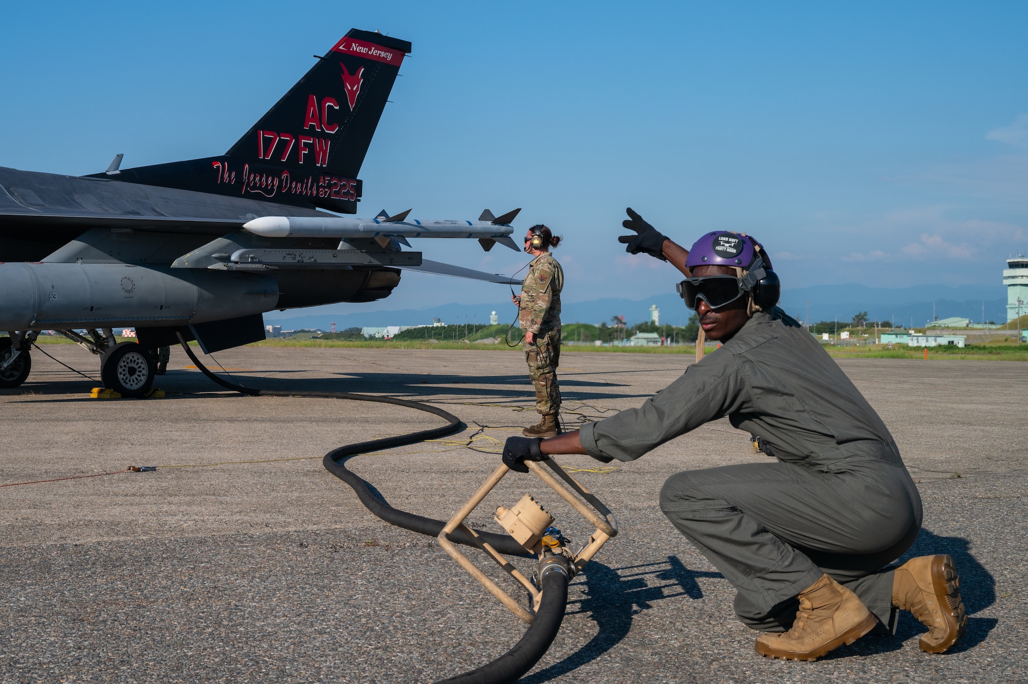 A Marine assists airmen with refueling procedures on an F-16 fighter jet.