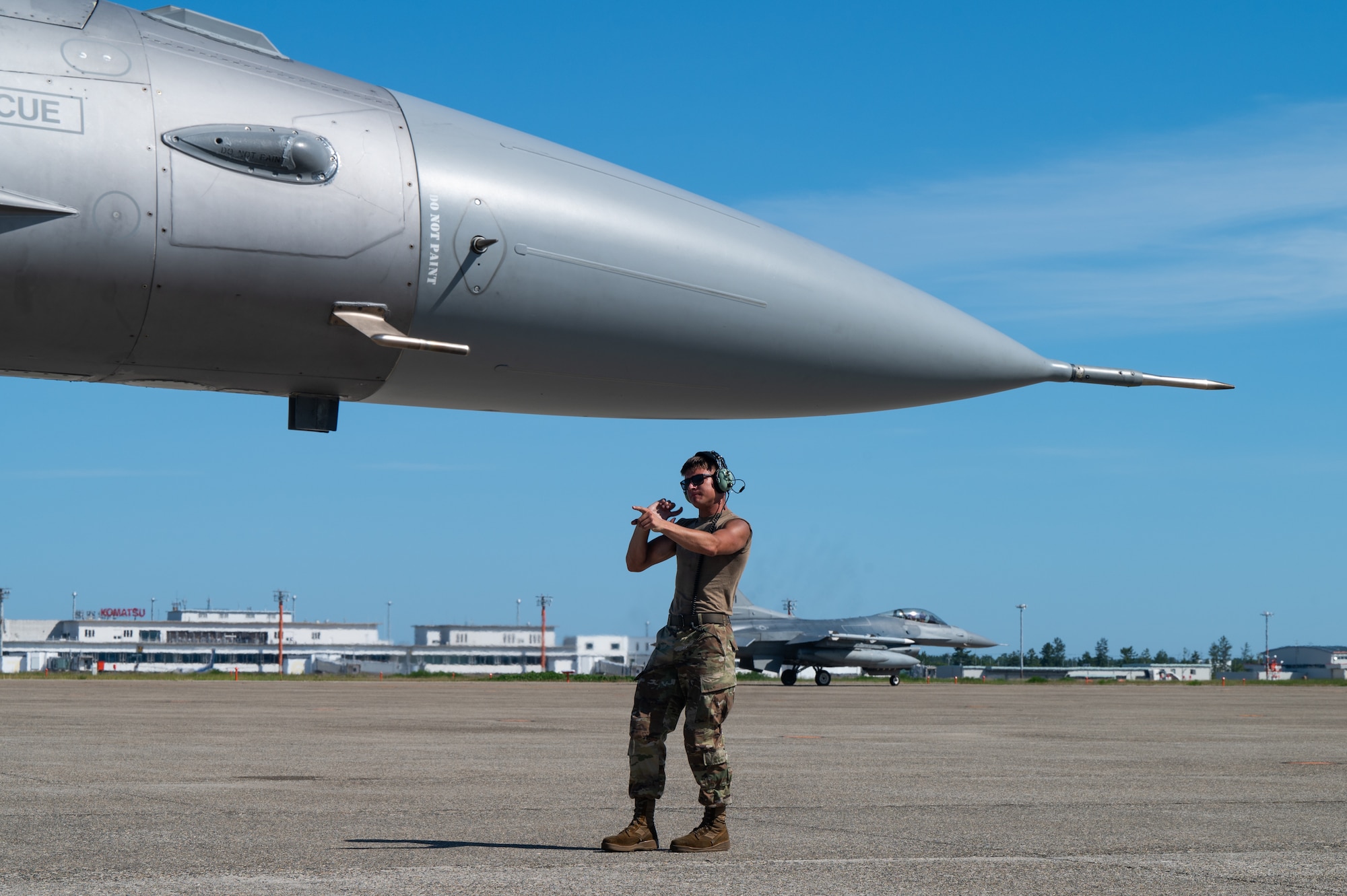 An aircraft maintainer marshals an F-16 fighter jet forward.
