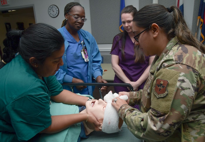 Two ladies wrap a gauze around a mannequin's head while two other ladies watch.