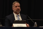 A person seated in a suit speaks to an audience.
