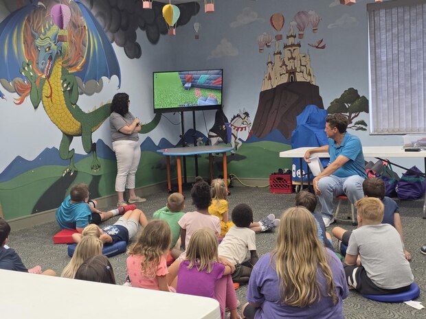 Children watch a video using a popular video game that demonstrates the functionality and application of circuits during "Storybook STEM" at the Camden County Library hosted by members of the Strategic Weapons Facility Atlantic (SWFLANT) and Trident Refit Facility’s STEM Teams.
