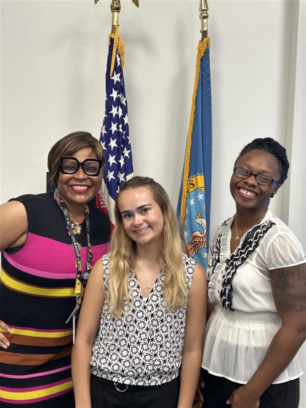 Three women pose in front of flags