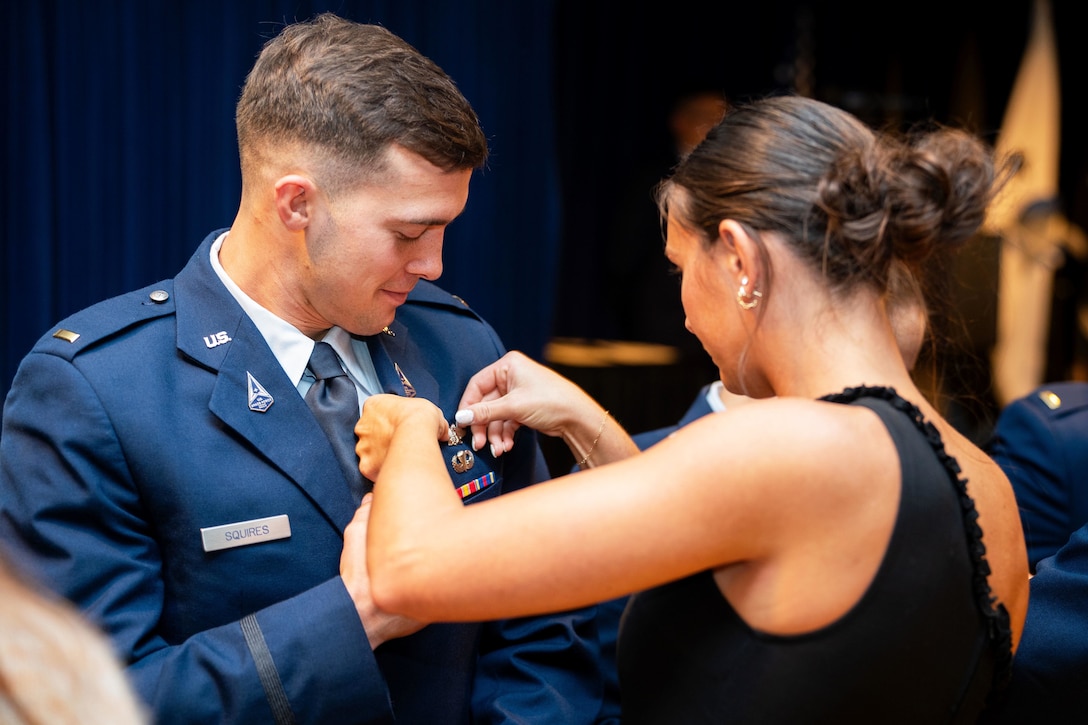 A guardian smiles as a loved one puts a badge on the lapel of their uniform.
