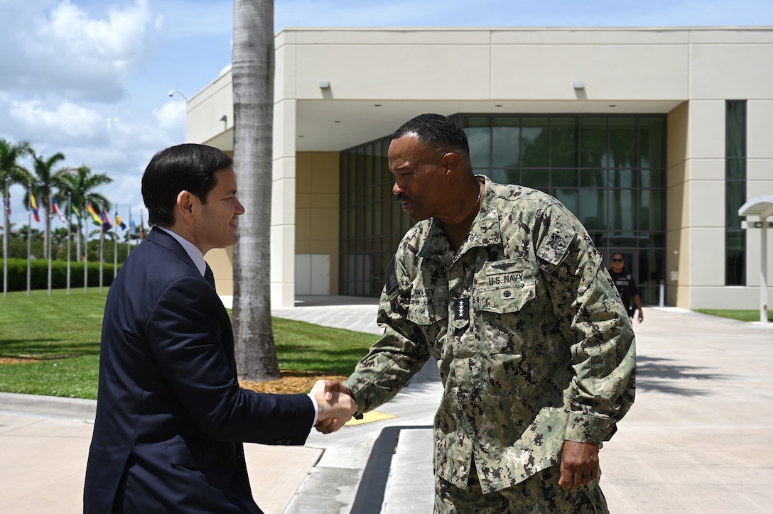 A man in dark blue suit shakes hands with a man in a camouflage uniform.