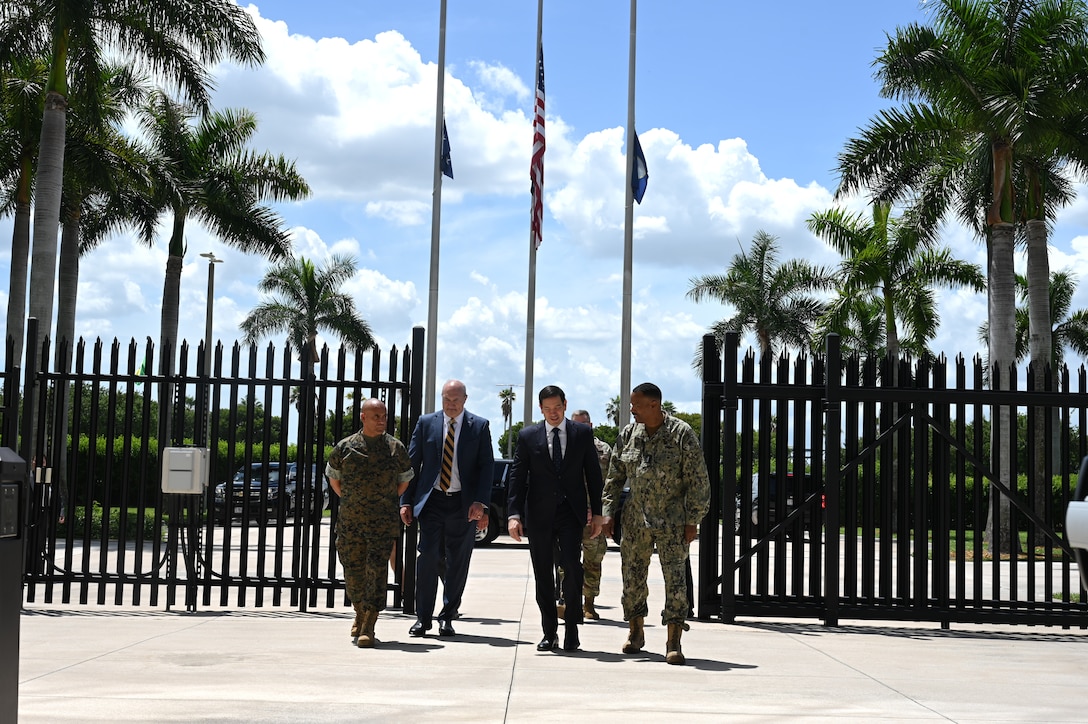 Four men in suits and camouflage uniforms walk together.