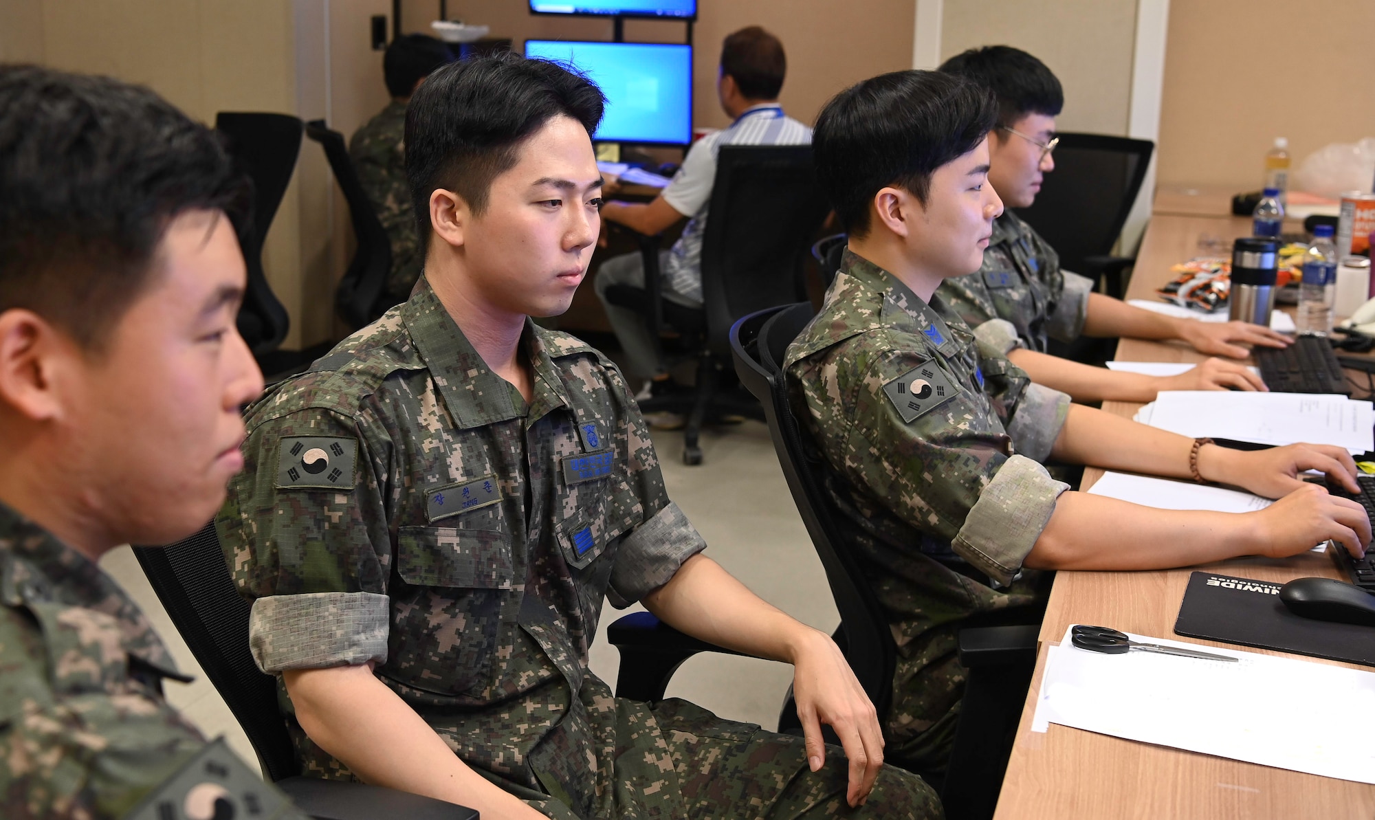 A group of people are sitting in front of a row of computers