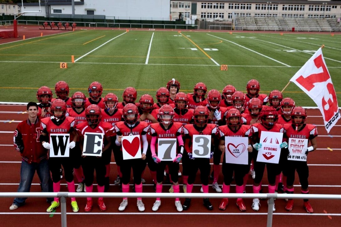 Kaiserslautern High School football players show support for teammate Aiden in 2024 by holding signs reading “We ♥ 73” during a game in Kaiserslautern, Germany. Aiden, a sophomore, collapsed during a game in September and was saved by two Army Reserve volunteers who provided emergency medical care. [Photo by Army Sgt. 1st Class Jessica Forester]