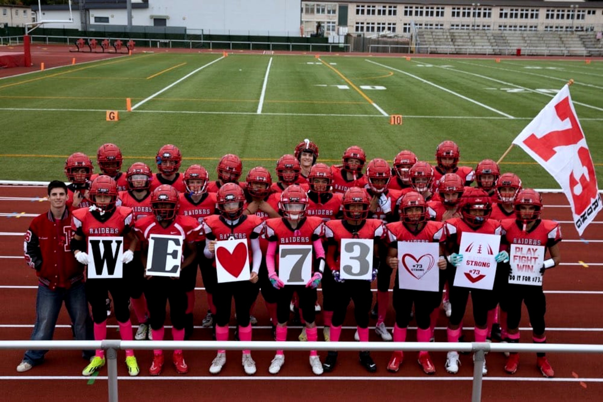 Kaiserslautern High School football players show support for teammate Aiden in 2024 by holding signs reading “We ♥ 73” during a game in Kaiserslautern, Germany. Aiden, a sophomore, collapsed during a game in September and was saved by two Army Reserve volunteers who provided emergency medical care. [Photo by Army Sgt. 1st Class Jessica Forester]