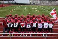 Kaiserslautern High School football players show support for teammate Aiden in 2024 by holding signs reading “We ♥ 73” during a game in Kaiserslautern, Germany. Aiden, a sophomore, collapsed during a game in September and was saved by two Army Reserve volunteers who provided emergency medical care. [Photo by Army Sgt. 1st Class Jessica Forester]