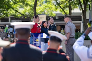 Three people stand and speak with their right hand raised as they face a man wearing a formal military uniform who also stands with his right hand raised.