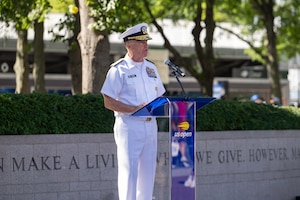 A man wearing a formal military uniform stands at a podium and speaks during an outdoor ceremony.