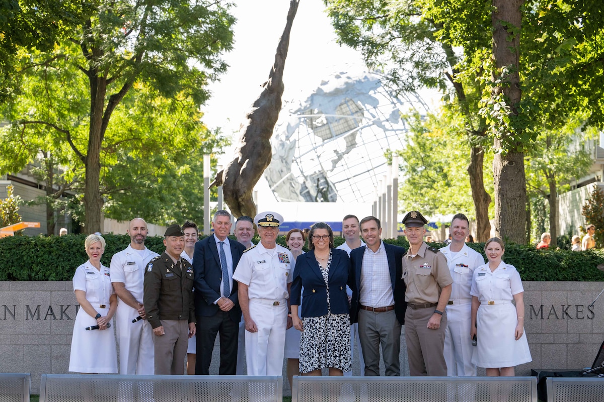 A group of people in assorted formal military uniforms poses with three people in business attire.