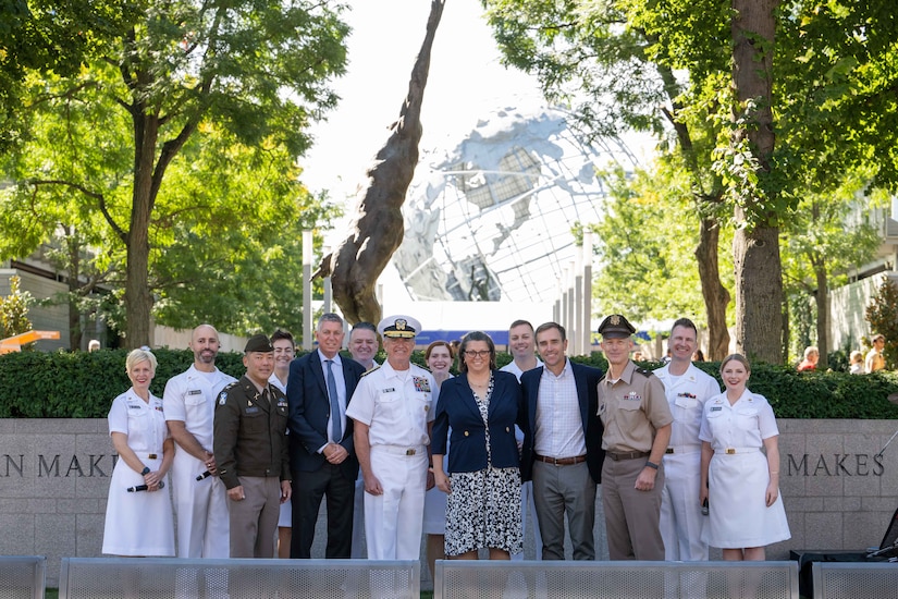 A group of people in assorted formal military uniforms poses with three people in business attire.