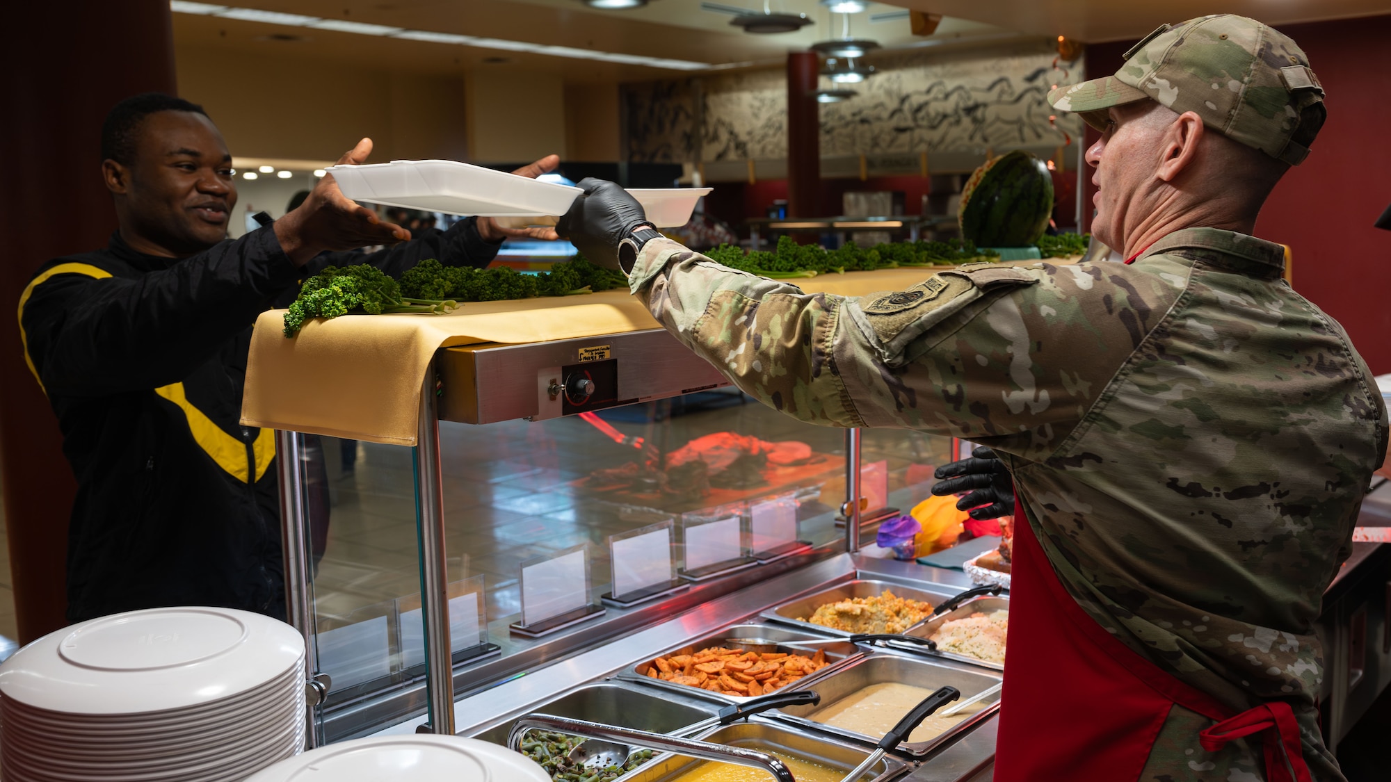 U.S. Air Force Col. Kevin Walsh, right, 51st Fighter Wing deputy commander, serves food during a Thanksgiving meal at Osan Air Base, Republic of Korea, Nov. 27, 2025. Leadership presence during the holiday served as a reminder that mission success begins with connected and supported Airmen. (U.S. Air Force photo by Senior Airman Rome Bowermaster)