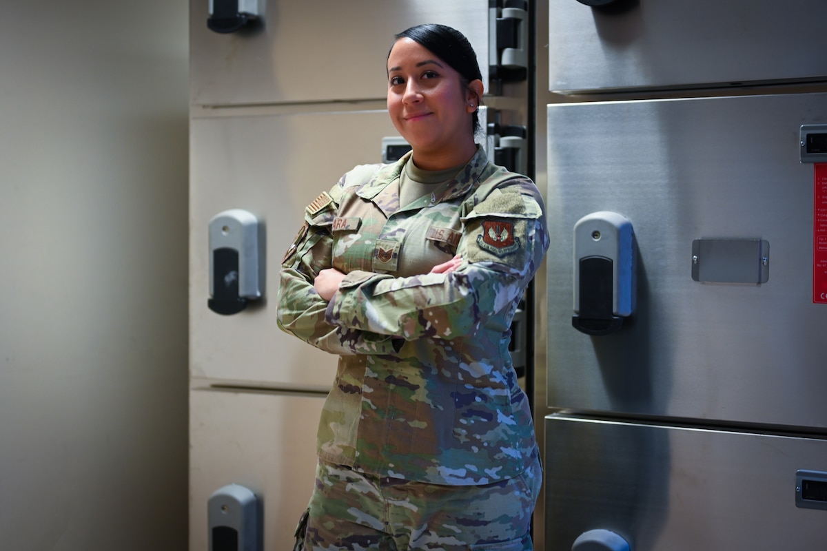 a military member standing in front of mortuary fridges with her arms crossed
