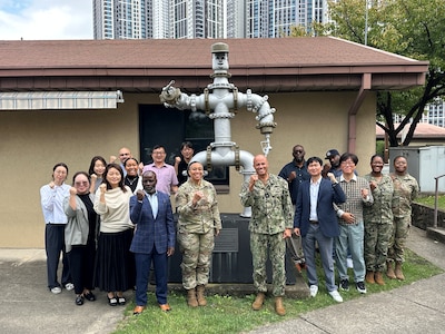 RDML George Bresnihan (center right) and Army Lt. Col. Jeremia Van (center left) gather around “Pipeman Pete” with staff at DLA Energy Indo-Pacific Korea headquarters. The statue, constructed with readily-available pipeline material, symbolizes esprit de corps among the petroleum workforce.