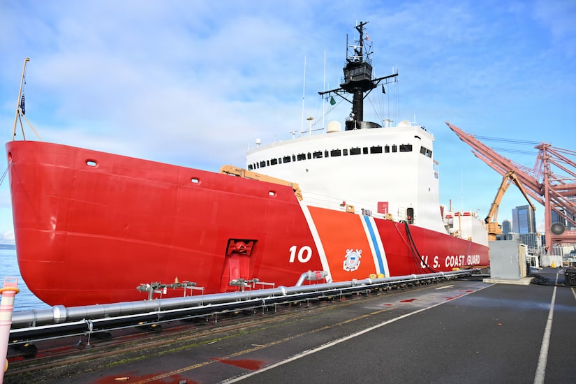A large red and white military ship is docked at a port.