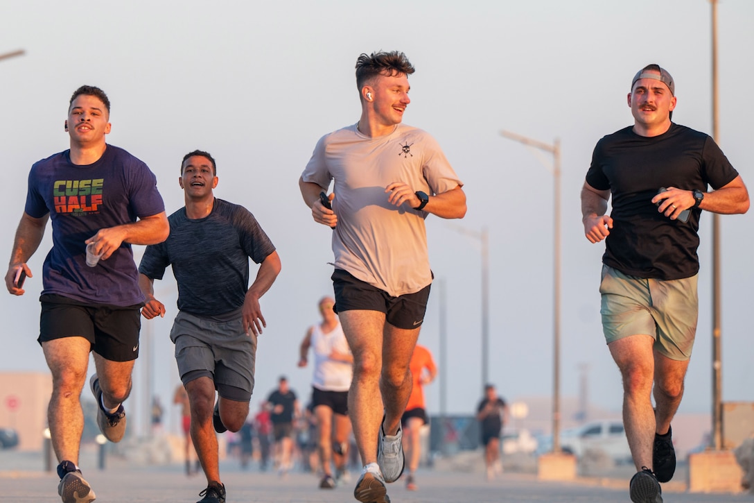 Service members in warm-weather workout clothes run outdoors during daytime.
