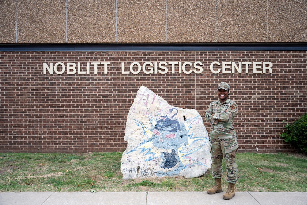 Person stands next to a rock outside.