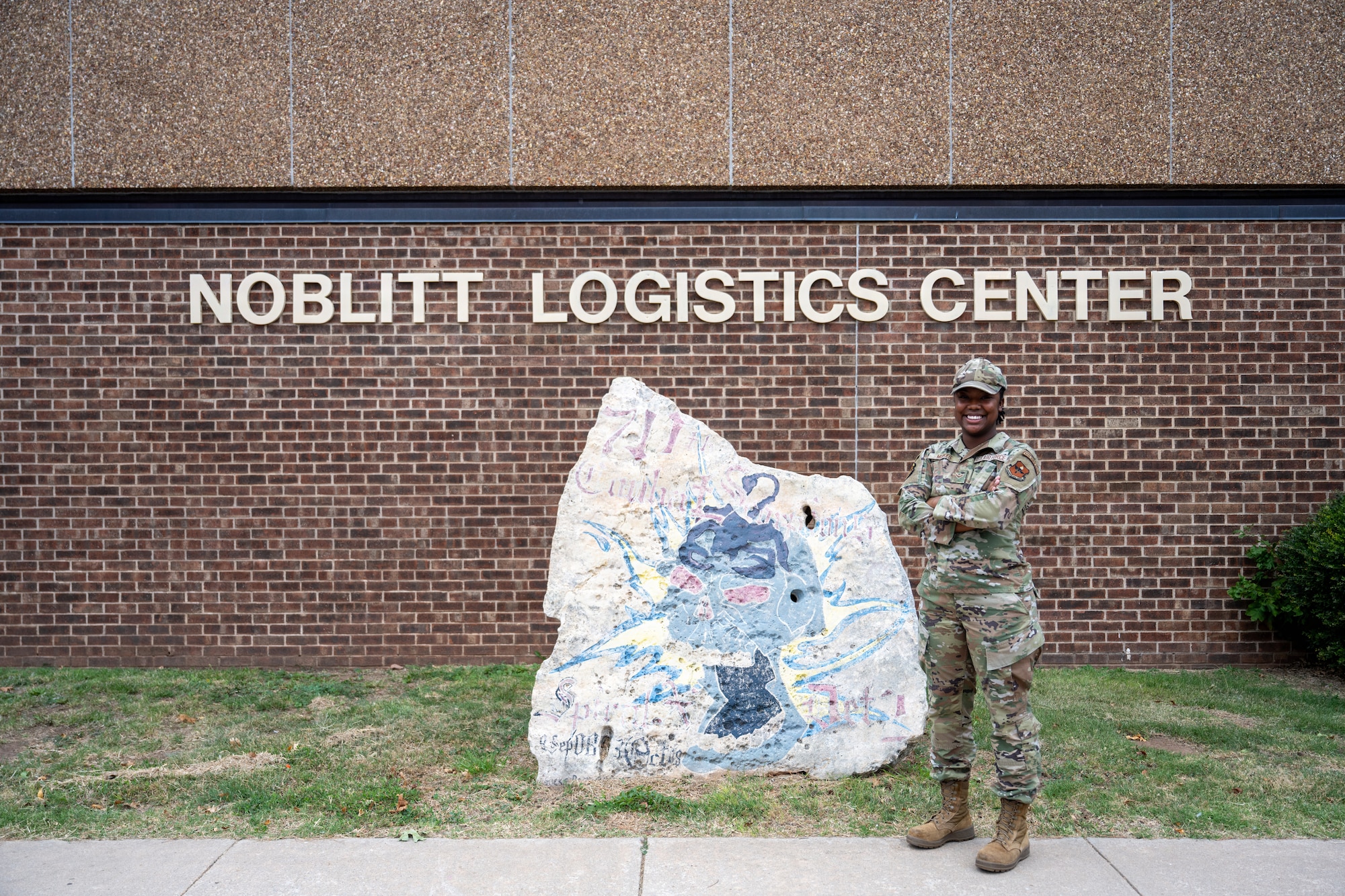 Person stands next to a rock outside.