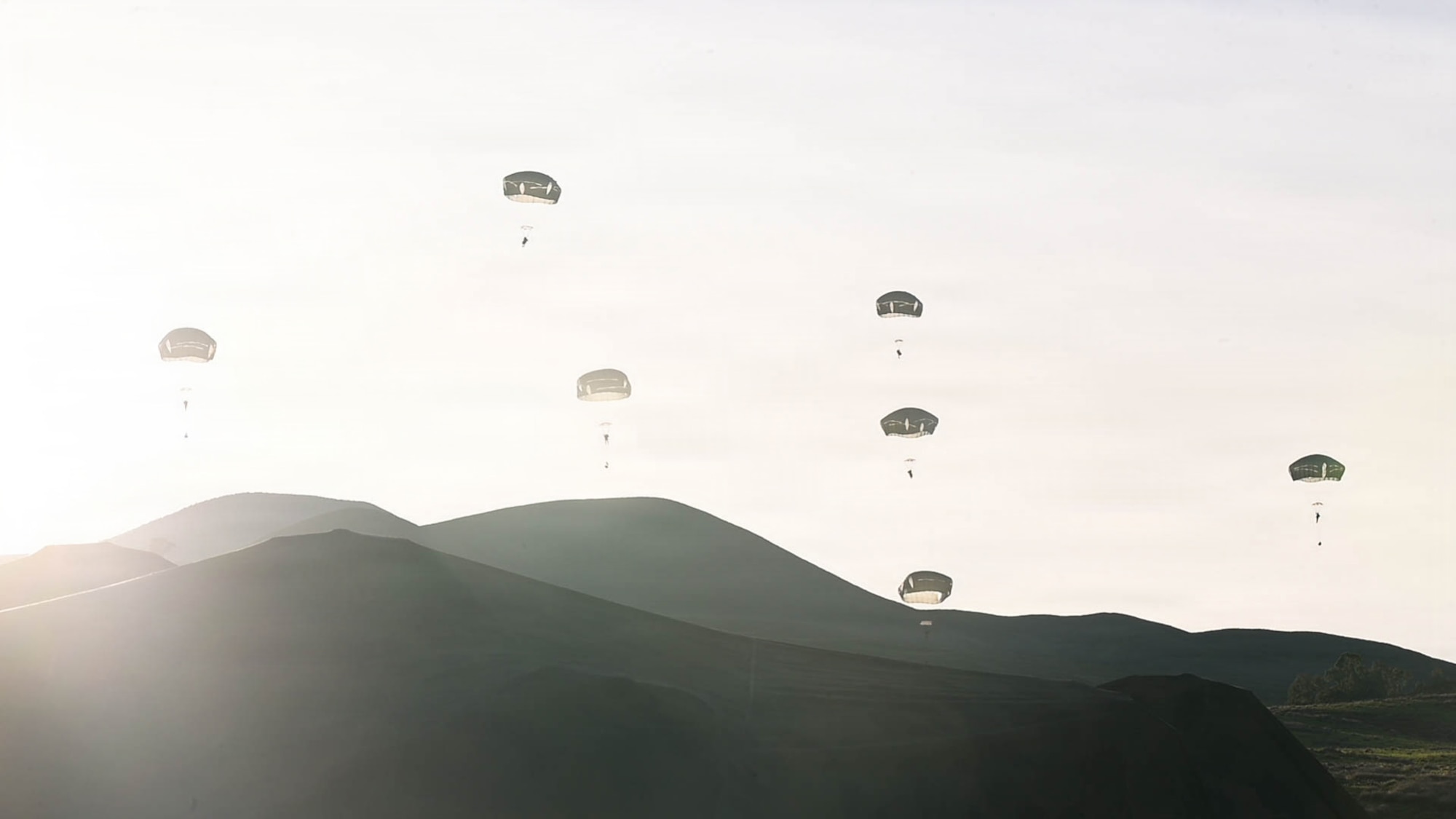 U.S. Army soldiers float towards the ground with parachutes.