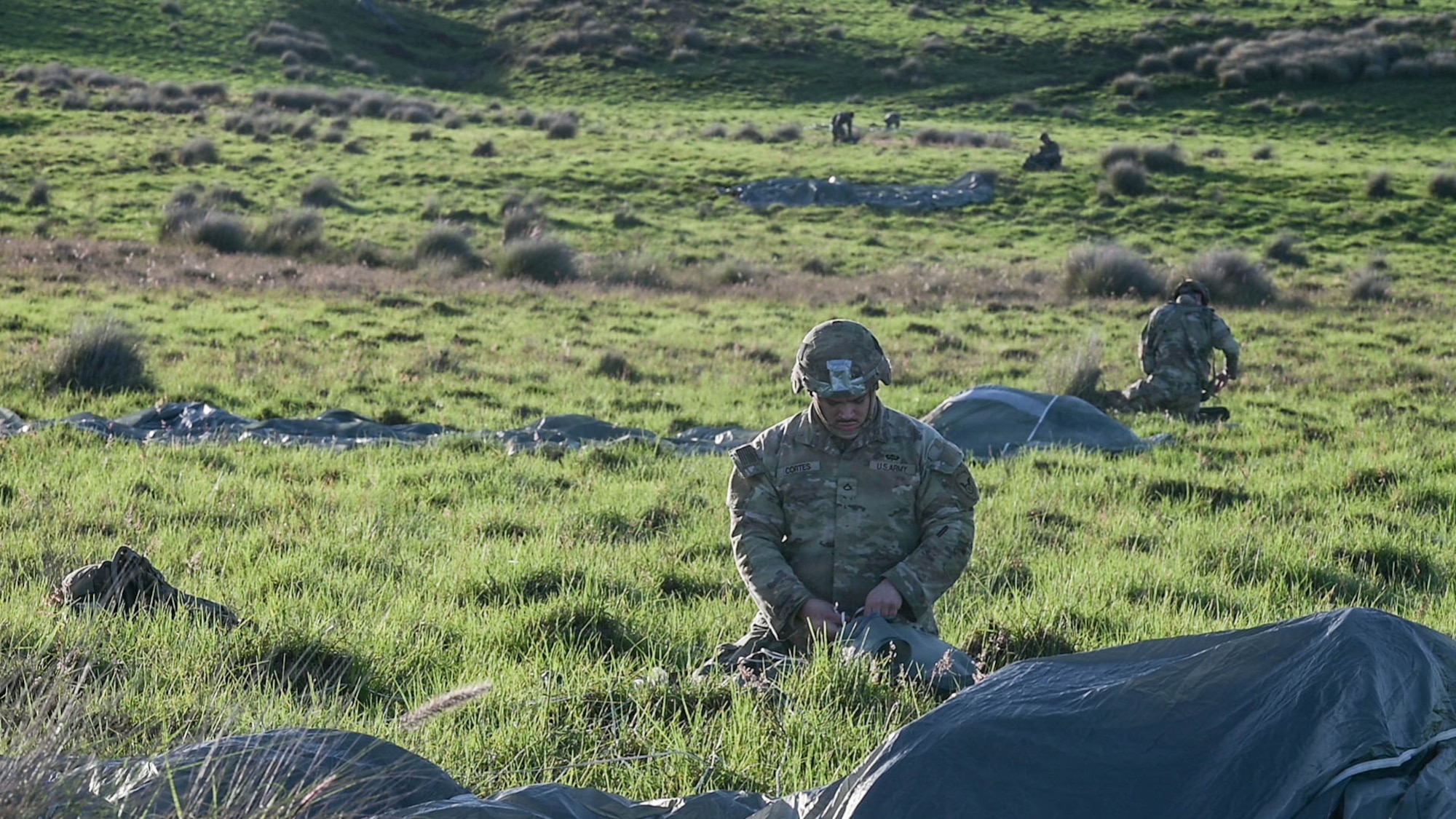 U.S. Army soldiers recover parachutes in a field.