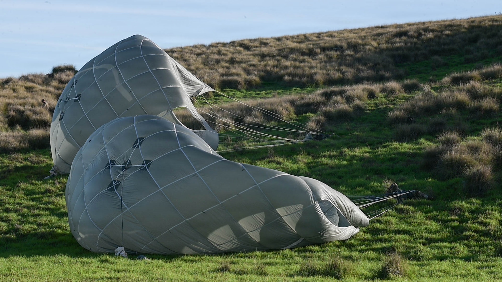 U.S. Army soldiers recover open parachutes on a hill.