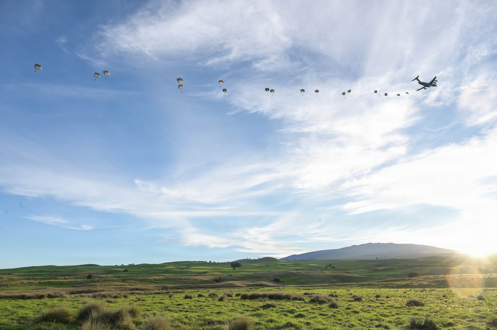 U.S. Air Force aircraft flies across a horizon with parachuted soldiers floating towards the ground.