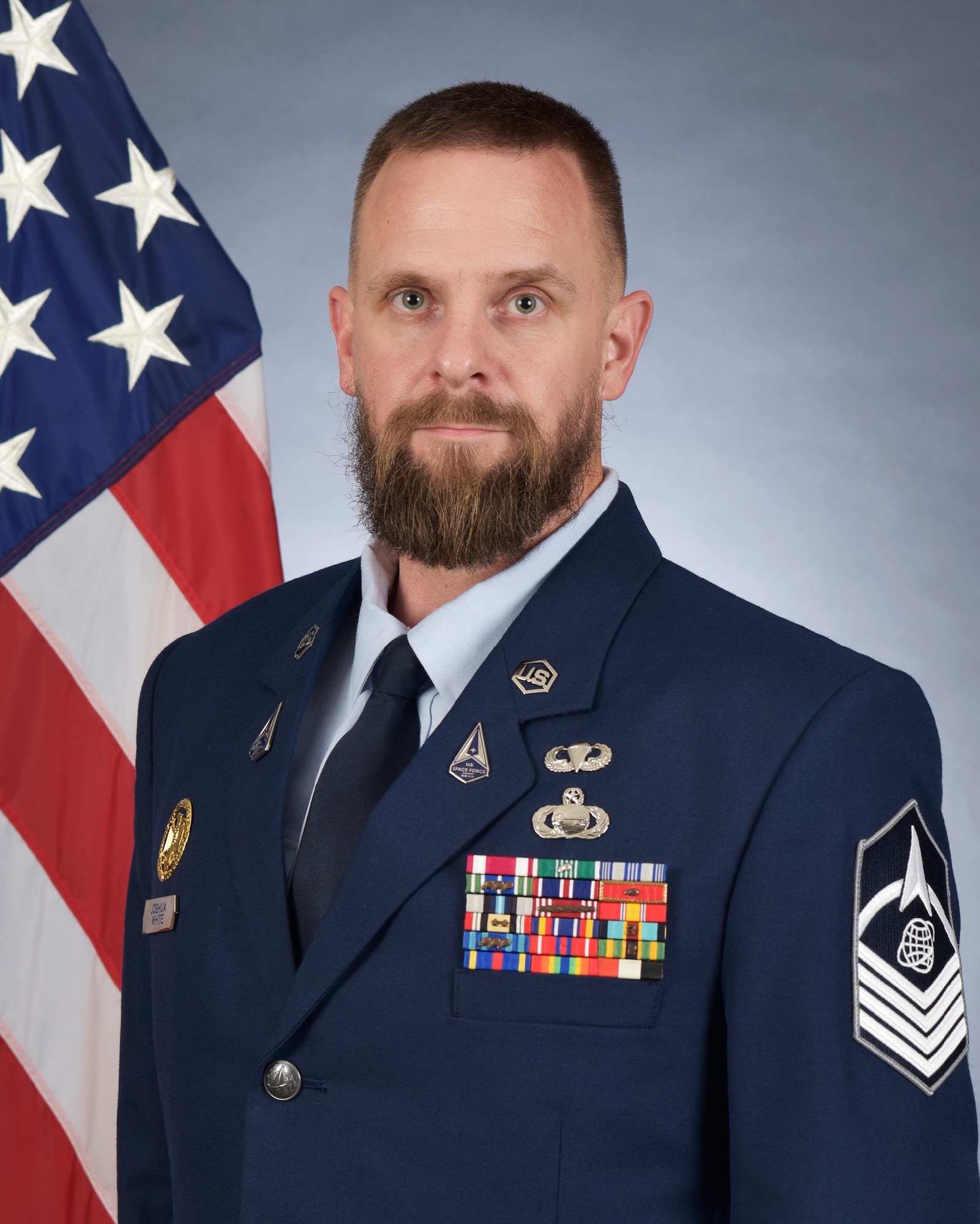 Master Sgt. Joshua White poses for an official photo wearing the Air Force standard blues dress uniform in front of an American flag.