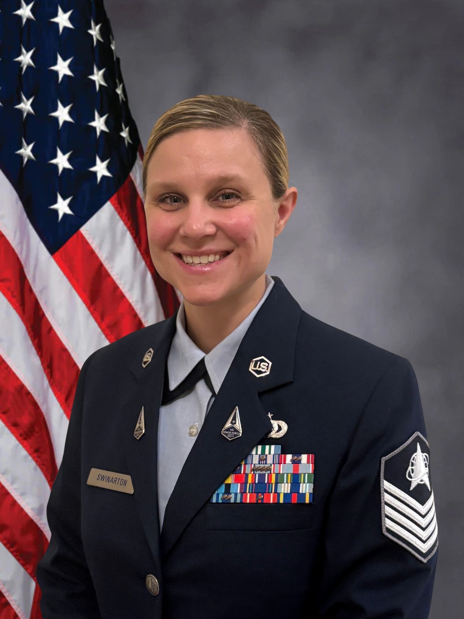 Tech. Sgt. Brandy Swinarton poses for an official photo wearing the Air Force standard blues dress uniform in front of an American flag.