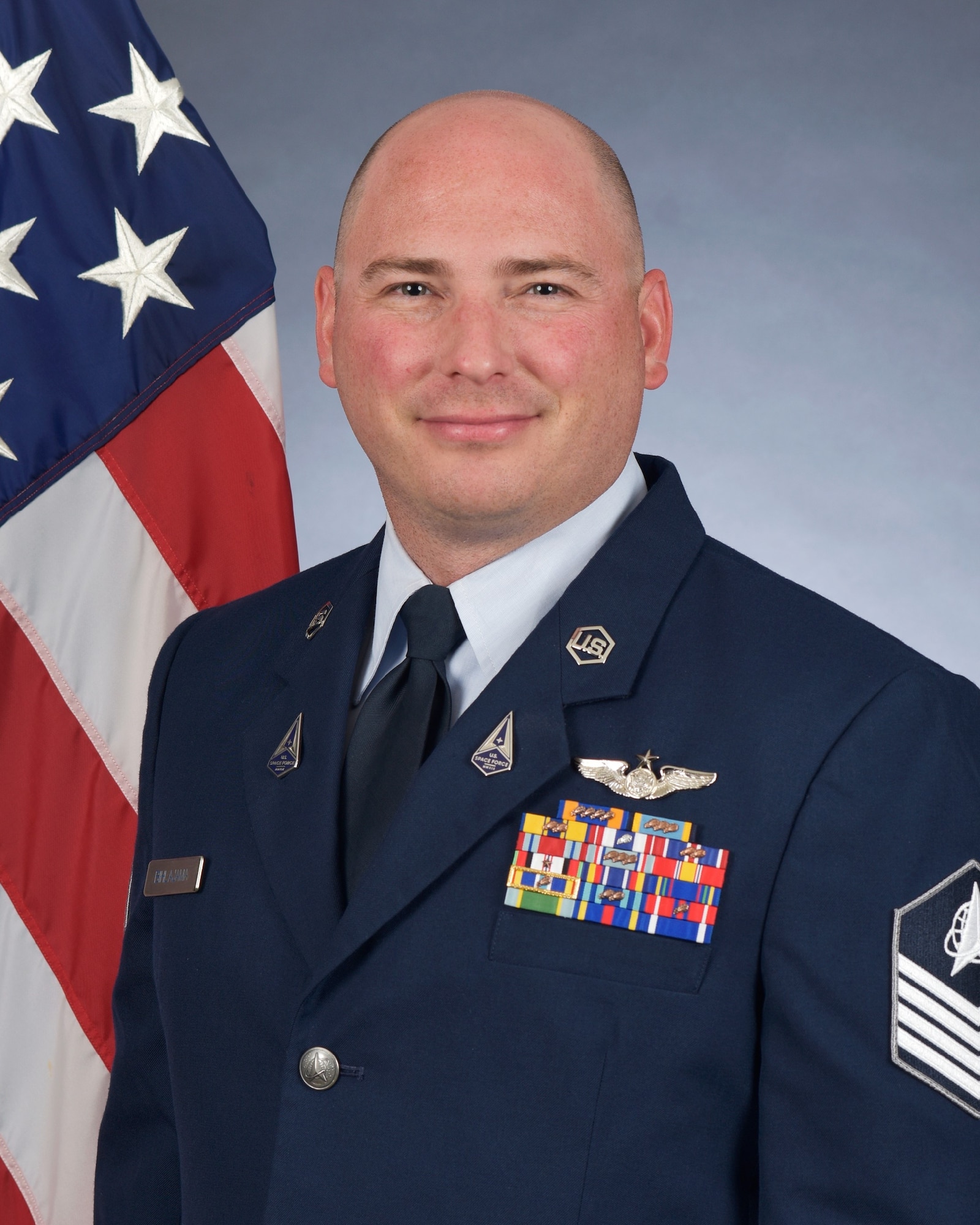 Tech. Sgt. Matthew Bihlajama poses for an official photo wearing the Air Force standard blues dress uniform in front of an American flag.