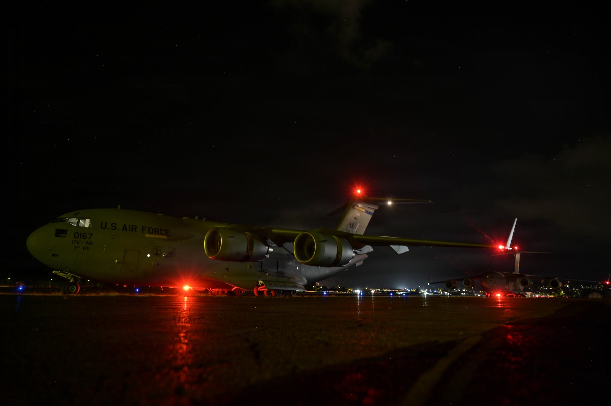 Two U.S. Air Force aircraft sitting on a flightline at night.