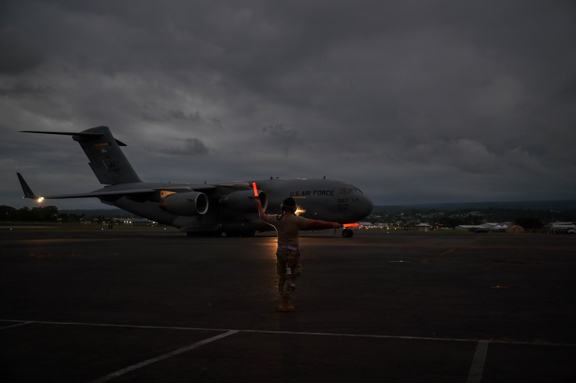 A U.S. Air Force soldier martialing an aircraft at night.