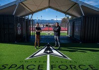 Two men stand in front of workout equipment outside.