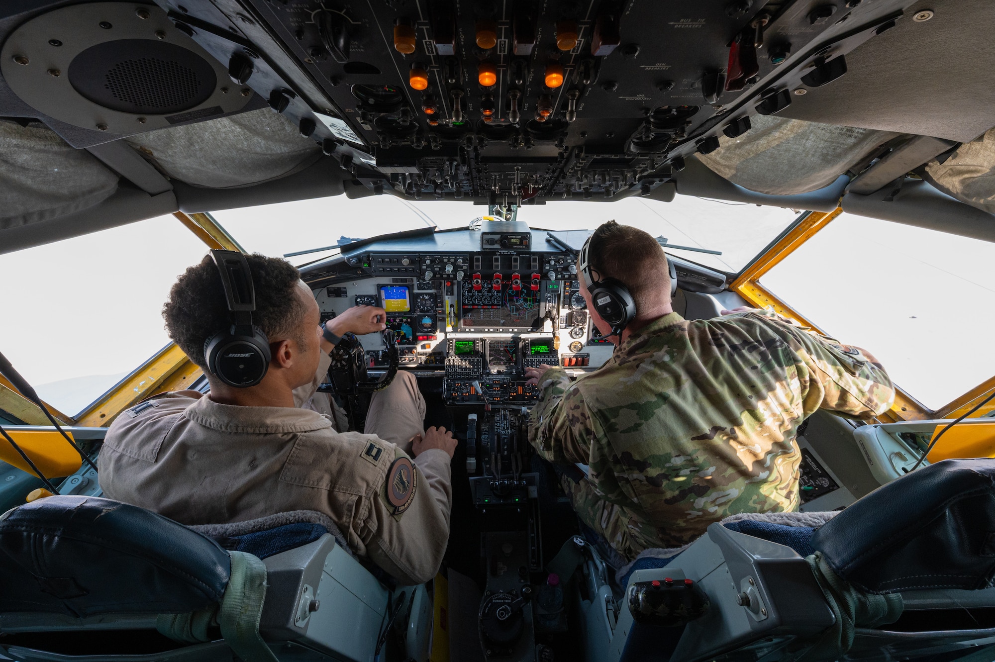 Two pilots sit in the cockpit of a KC-135 Stratotanker aircraft looking over the panels in preparation for flight