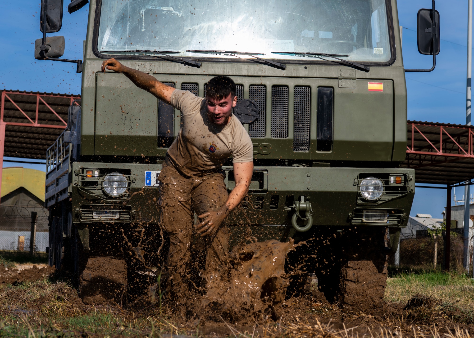 A Spanishserive member splashes through a mud obstacle