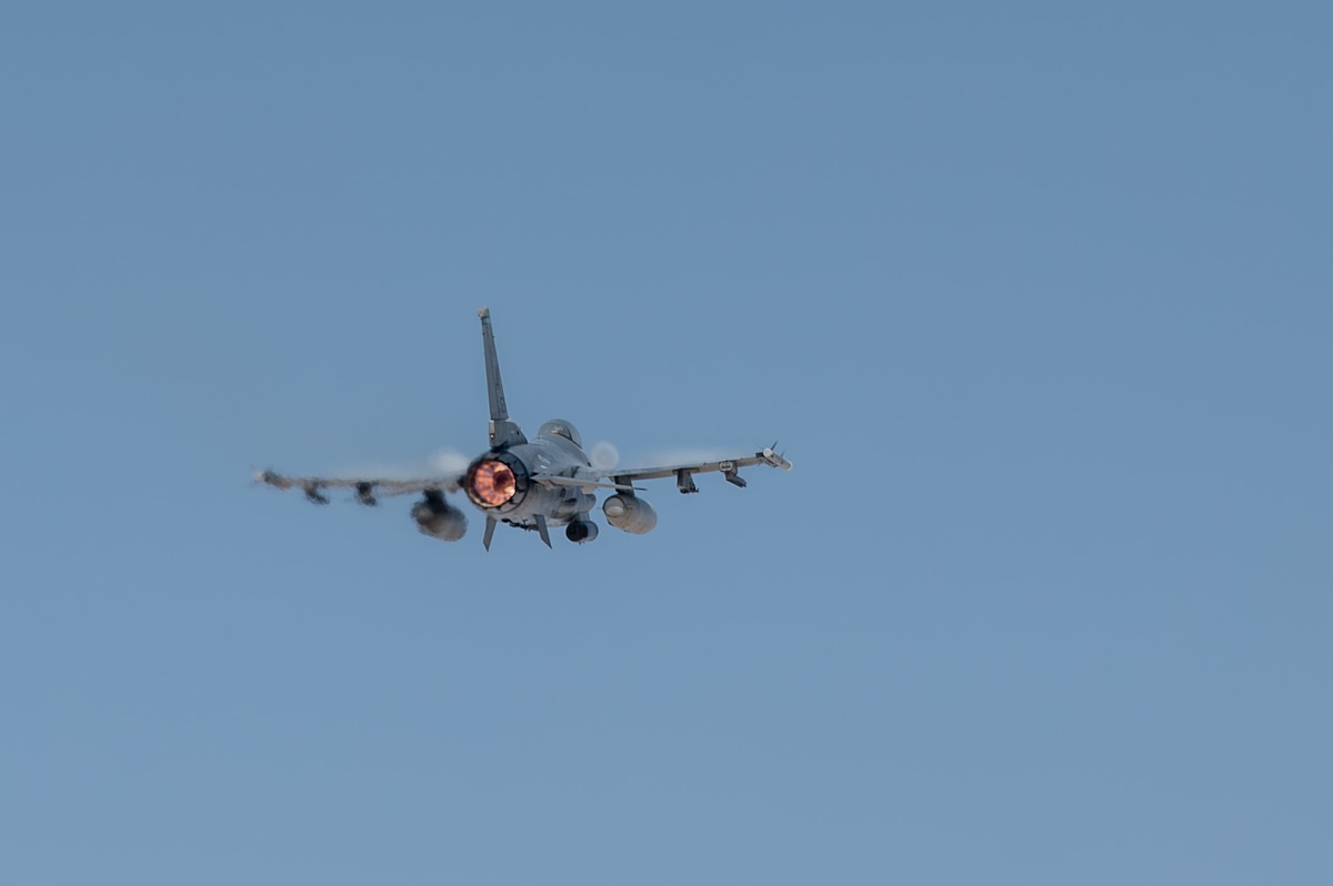 An F-16 Fighting Falcon aircraft flies away. The afterburner is light up.