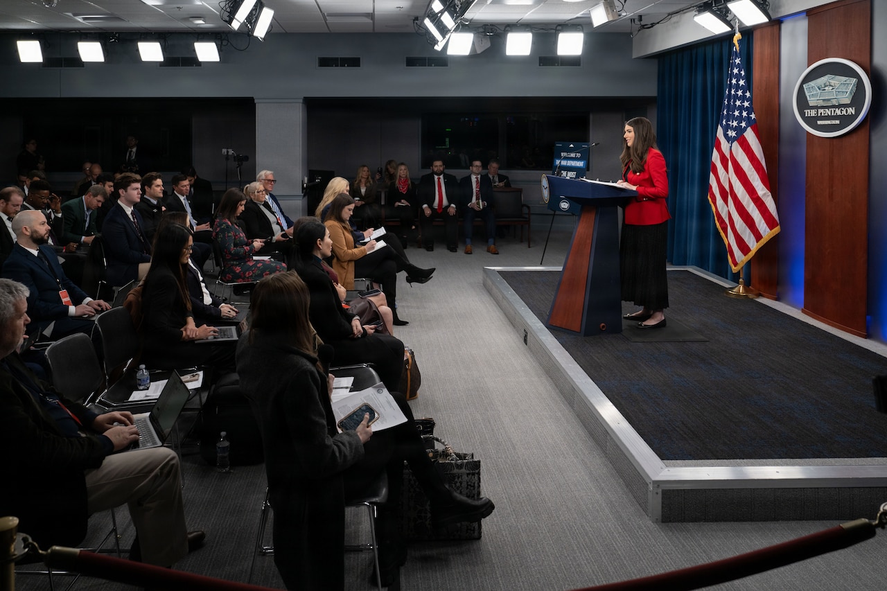 A person speaks from a podium to a seated audience.