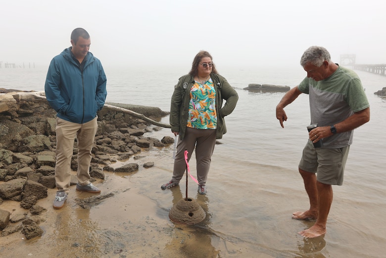 two men and one woman stand in water looking at a 3-d printed oyster reef