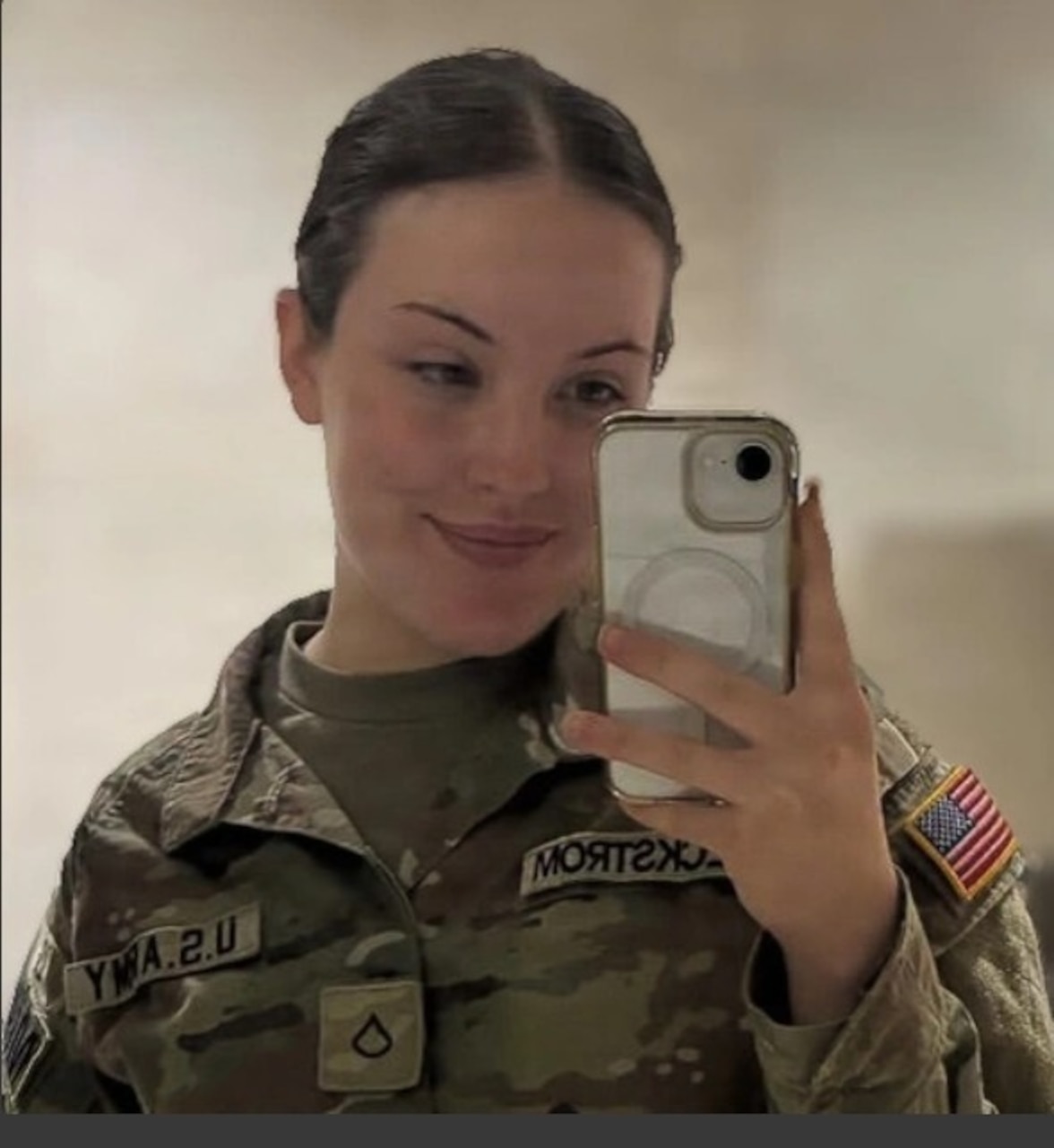 A woman in a camouflage military uniform takes a photo with her cellphone.
