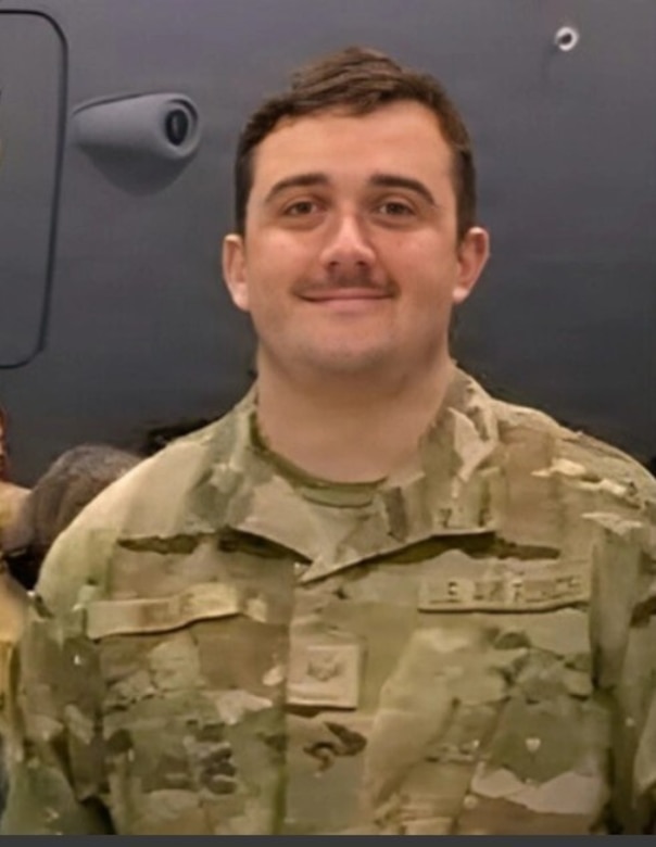 A man in a camouflage military uniform smiles for a photo.