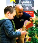 Ethan Coates, 6, affixes an ornament honoring a fallen service member on the tree with help from his father, Matt Coates.
