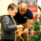 Ethan Coates, 6, affixes an ornament honoring a fallen service member on the tree with help from his father, Matt Coates.