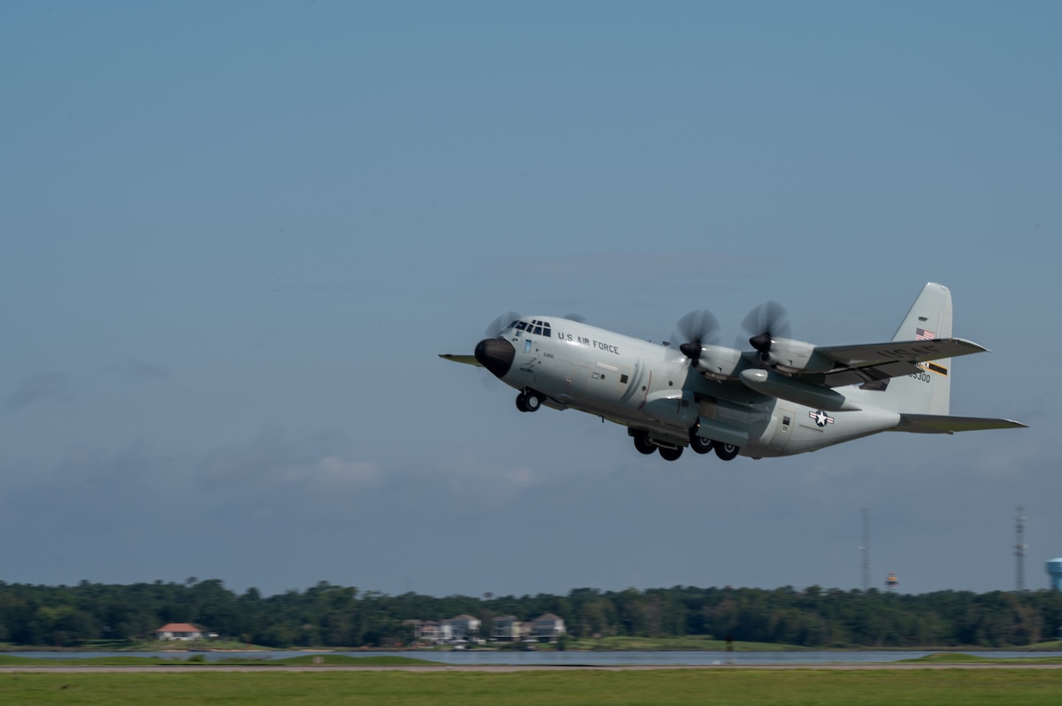 A large gray military aircraft takes off from a runway during daytime.
