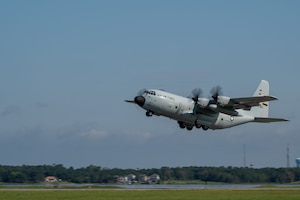 A large gray military aircraft takes off from a runway during daytime.
