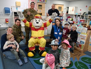 Sparky the Fire Dog entertains children at the child development center during Fire Prevention Week at RAF Mildenhall, England, Oct. 7, 2025. Sparky brought along some of his firefighter friends from the 100th Civil Engineer Squadron Fire Department who read fire-related stories to children in multiple classes, talked to them about fire safety, and gave out plastic fire helmets.