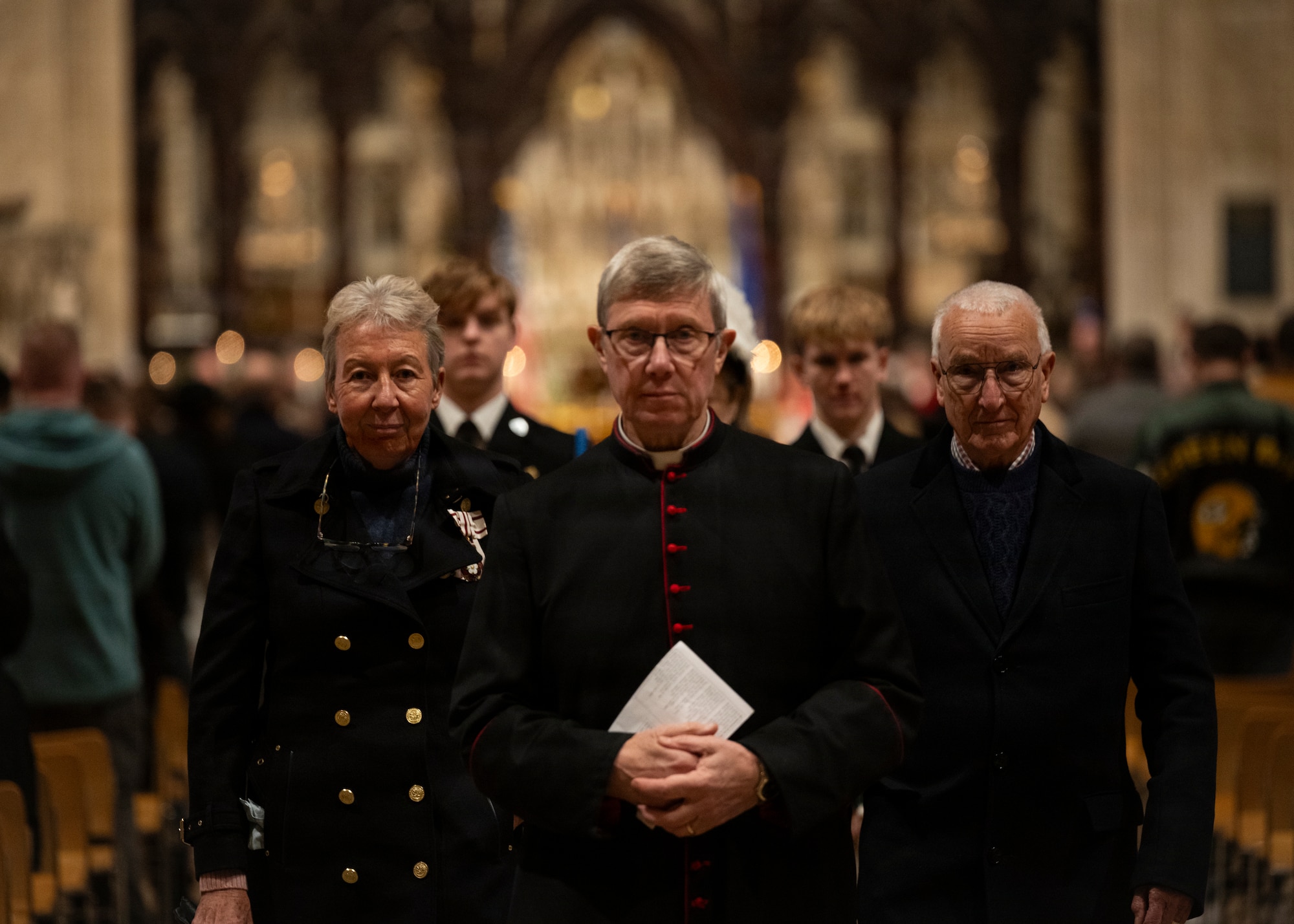 From left, His Majesty’s Lord Lieutenant of Cambridgeshire, Julie Spence OBE CStJ QPM, The Very Revd Mark Bonney D.L., and John Spence, walk down an aisle at Ely Cathedral, Nov. 26, 2025. British and American nationals attended a Thanksgiving service held for U.S. service members stationed in the U.K. (U.S. Air Force photo by Staff Sgt. Nash Truitt)
